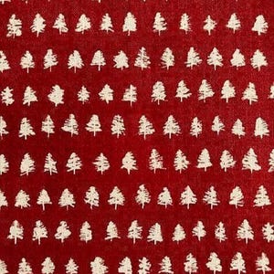 May include: A deep red fabric featuring a repeating pattern of small, off-white stylized evergreen trees arranged in horizontal rows. The material has a visible woven texture, and the tree shapes appear slightly distressed or brush-stroked.
