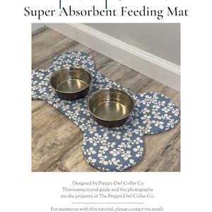 May include: A bone-shaped pet placemat featuring a blue fabric with a white leaf pattern. Two circular stainless steel bowls are placed on top of the mat. The text Pet Placemat Super Absorbent Feeding Mat is visible above the mat.