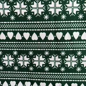 May include: A close-up of a fabric with a repeating pattern of white snowflakes, hearts, and diamond shapes on a dark green background. The design has a folk art or Scandinavian aesthetic.