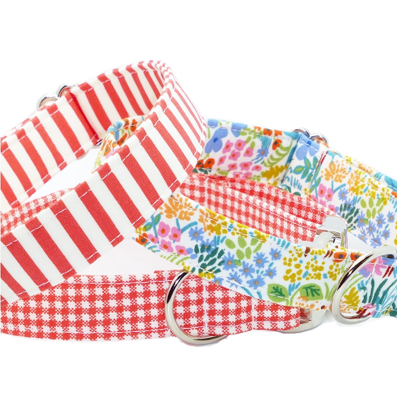 May include: Three pet collars featuring distinct patterns: one with bold red and white vertical stripes, one with a red and white gingham check, and one with a colorful floral print on a white background, each equipped with silver metal D-rings.