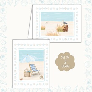 May include: Set of two beach-themed greeting cards. Each card features a watercolor illustration of a beach scene with a blue sky, sand, and a border of stars and seashells. One card shows a seagull, the other a beach chair.