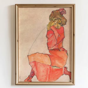 Peut inclure: Œuvre d'art encadrée représentant une figure assise dans des tons rouges et oranges. La figure a une main sur le visage, et l'œuvre est placée sur un fond neutre. Le cadre est de couleur marron clair.