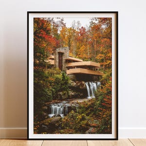 Könnte beinhalten: Ein gerahmter Druck eines Hauses, das über einem Wasserfall gebaut wurde. Das Haus hat eine Steinfassade und Holzbalkone. Der umliegende Wald zeigt Herbstfarben. Der Wasserfall stürzt über Felsen und schafft eine ruhige Landschaft.
