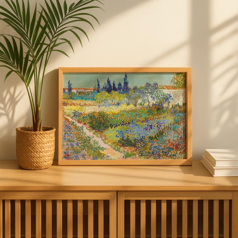 May include: A framed landscape painting with a wooden frame. The artwork depicts a colorful garden scene with a path, trees, and flowers. The painting is displayed on a wooden cabinet, with a potted plant and books nearby.