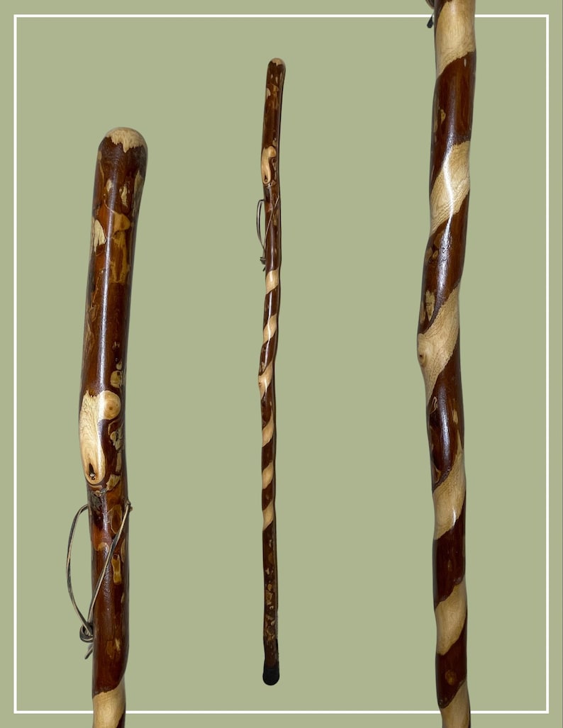 May include: A tall wooden walking stick featuring a polished finish with a distinct spiral pattern of dark brown and light tan wood grain. The staff has a smooth, rounded top and a small leather cord loop attached near the upper section of the shaft.