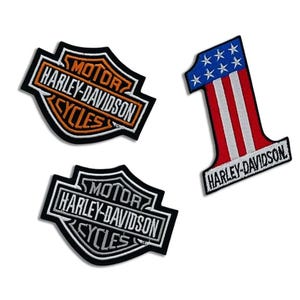 Peut inclure: Trois écussons Harley-Davidson. Deux écussons présentent le logo Harley-Davidson en noir et orange, et en noir et blanc. Le troisième écusson est un numéro un en rouge, blanc et bleu avec le logo Harley-Davidson.