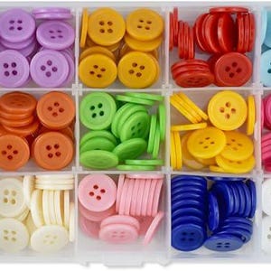 Op de afbeelding: Een doorzichtige plastic organizer gevuld met diverse kleurrijke naaiknopen. De knopen zijn in tinten bruin, paars, geel, rood, blauw, groen, oranje, roze, wit en zwart. Elke kleur is gescheiden in een eigen compartiment.