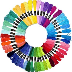 Puede incluir: Una disposición circular de madejas de hilo de bordar de colores. El hilo está dispuesto en un patrón de arcoíris, con colores que van del amarillo al morado, rojo y azul. Cada madeja tiene una etiqueta en blanco y negro.