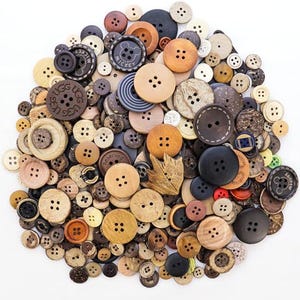 May include: A collection of various buttons in different sizes, colors, and materials. The buttons include wooden, plastic, and fabric-covered options, with a range of colors from light beige to dark brown and black. Some buttons have four holes, while others have two.