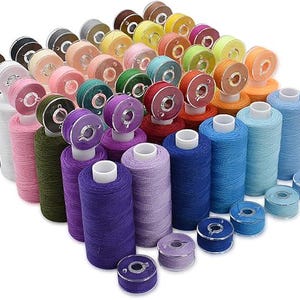 Peut inclure: Un assortiment de bobines de fil à coudre et de canettes colorées. Les bobines sont de différentes couleurs, dont le noir, le blanc, le rose, le vert, le violet, le bleu et l'orange. Les canettes sont de couleurs assorties.