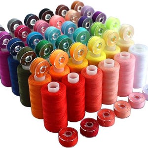 May include: A collection of colorful sewing thread spools and bobbins. The spools are arranged in a neat display, showcasing a variety of colors including red, orange, yellow, green, blue, pink, and purple. The bobbins are in matching colors.