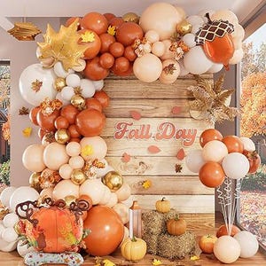 Puede incluir: Un arco de globos con temática otoñal en tonos naranja, marrón y blanco, con una gran hoja dorada y un globo de bellota. Las palabras "Fall Day" se muestran en un fondo de madera, con calabazas y balas de heno.