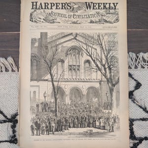 Puede incluir: Una copia antigua de Harper's Weekly, Journal of Civilization, fechada el 15 de mayo de 1869. La portada presenta una ilustración detallada en blanco y negro de un grupo de personas frente a un edificio.