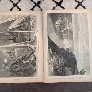 May include: An open book displaying two monochrome illustrations. One page shows three figures in historical attire. The other depicts a landscape with a waterfall and cliffs. The pages show signs of age and wear.