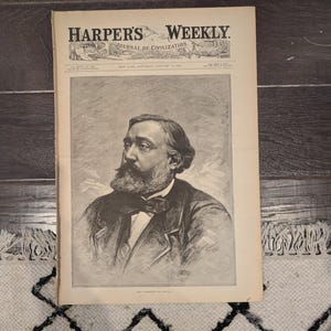 May include: An antique copy of Harper's Weekly, Journal of Civilization, from January 1888. The cover features a detailed black and white portrait of a man with a beard and bow tie. The newspaper is on a patterned rug.