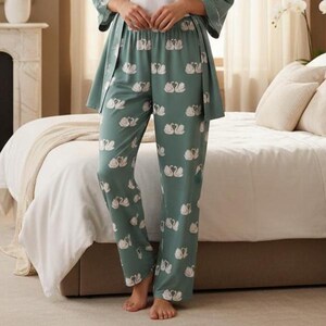 Puede incluir: Pantalones de pijama verdes con un estampado de cisnes blancos. Los pantalones forman parte de un conjunto a juego y est&aacute;n hechos de una tela suave y fluida. Los cisnes est&aacute;n dispuestos en un patr&oacute;n repetido.