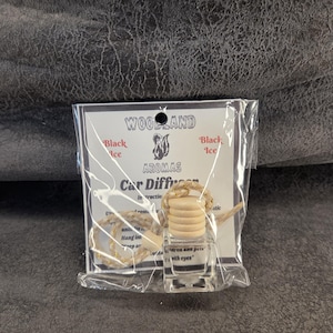May include: A clear glass car diffuser bottle with a light-colored wooden cap and a braided hanging cord, packaged in a clear plastic bag with a white label featuring the text Woodland Aromas Black Ice Car Diffuser and a squirrel illustration.
