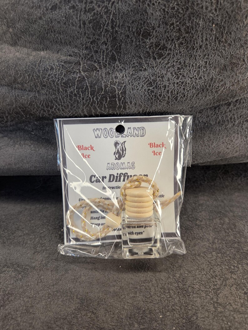 May include: A clear glass car diffuser bottle with a light-colored wooden cap and a braided hanging cord, packaged in a clear plastic bag with a white label featuring the text Woodland Aromas Black Ice Car Diffuser and a squirrel illustration.