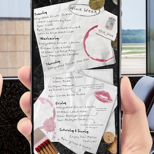 May include: A smartphone displays a handwritten itinerary for a wine-themed event, with details like "Wine Week," locations, and times. The screen shows notes, wine stains, and a lipstick mark. A hand holds the phone.