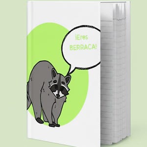May include: A white notebook featuring a cartoon raccoon. The raccoon is grey with a black mask and is positioned in front of a light green circle. A speech bubble says "¡Eres BERRACA!"