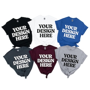 May include: A collection of six short-sleeved t-shirts in various colors: black, white, blue, charcoal, burgundy, and gray. Each shirt features the text "YOUR DESIGN HERE" in a bold, white font, centered on the front.