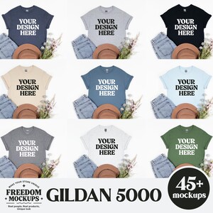 Può includere: Nove magliette Gildan 5000 in vari colori, ciascuna con "YOUR DESIGN HERE" stampato in bianco. Le magliette sono esposte con jeans, un cappello marrone e accenti floreali. L'immagine include anche il testo "FREEDOM + MOCKUPS" e "GILDAN 5000".