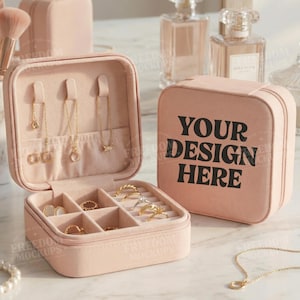 Puede incluir: Una caja de joyer&iacute;a rosa, abierta para exhibir anillos y collares. La caja es cuadrada con cierre de cremallera. El texto "YOUR DESIGN HERE" est&aacute; impreso en la caja cerrada. Se ven collares y anillos dorados dentro de la caja.