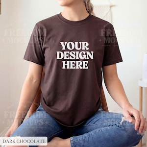 May include: A dark chocolate-colored t-shirt with the text "YOUR DESIGN HERE" in white block letters. The shirt is a short-sleeved crew neck style. The model is wearing blue jeans. The words "DARK CHOCOLATE" are at the bottom of the image.