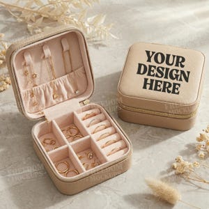 Puede incluir: Joyero beige con cremallera dorada y el texto "YOUR DESIGN HERE". La caja abierta revela un interior rosa con compartimentos para anillos, pendientes y collares. Se exhiben joyas de oro en el interior.
