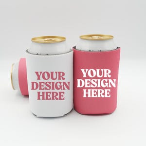 Könnte beinhalten: Drei Getränkedosenkühler in Weiß und Rosa. Der weiße Kühler hat den Text "YOUR DESIGN HERE" in Rosa. Der rosa Kühler hat denselben Text in Weiß. Die Dosen sind goldfarben und weiß.