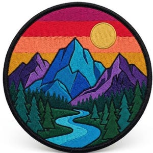 May include: Embroidered patch featuring a mountain landscape with a river, trees, and a setting sun. The design includes shades of blue, purple, green, orange, and red. The patch is round with a black border.