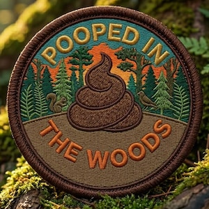 May include: Round embroidered patch with the text "POOPED IN THE WOODS". The patch features a brown poop emoji, trees, and a squirrel. The patch has a brown border and is set against a forest background.