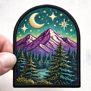 May include: Embroidered patch featuring a mountain landscape under a starry night sky. The design includes purple mountains, green pine trees, a crescent moon, and stars. The patch has a black border and is held by a hand.