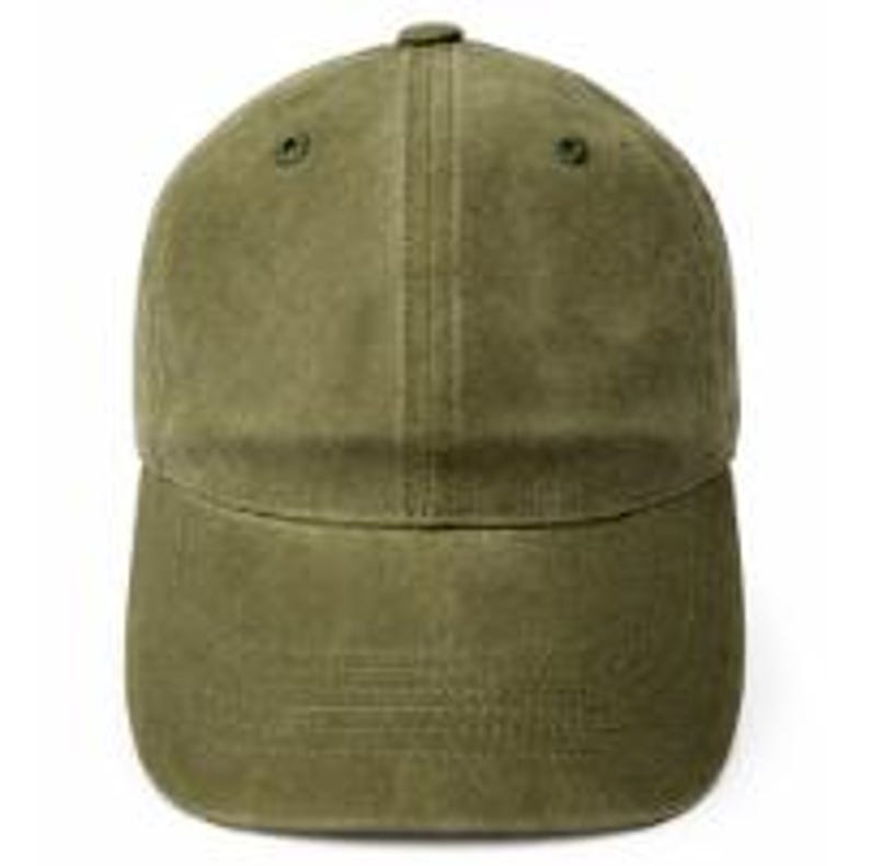 Puede incluir: Una gorra de b&eacute;isbol de color verde oliva con una construcci&oacute;n de seis paneles, visera curva y ojales cosidos a juego en la corona. El tejido tiene una textura suave y mate, y la gorra presenta una costura vertical central.
