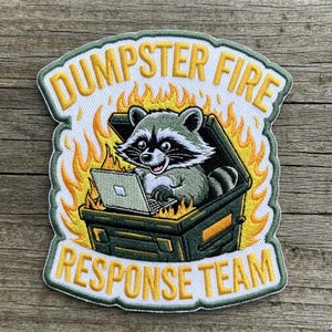May include: Embroidered patch featuring a raccoon working on a laptop inside a dumpster engulfed in flames. The patch reads "Dumpster Fire Response Team" in yellow and white lettering, with a green border.