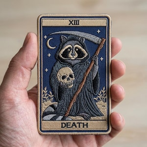 May include: Embroidered patch featuring a raccoon dressed as the Grim Reaper, holding a skull and scythe. The design is a tarot card with the word "DEATH" at the bottom and "XIII" at the top. The patch has a blue background with a tan border.
