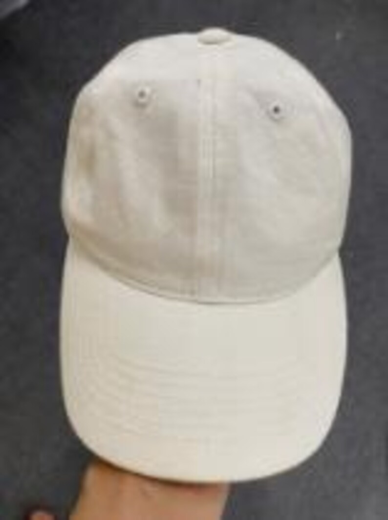 Puede incluir: Una gorra de b&eacute;isbol de color blanco roto liso con una corona estructurada de seis paneles, ojales bordados a juego y una visera curva. La gorra est&aacute; confeccionada en tela lisa e incluye una costura vertical central en el panel frontal.