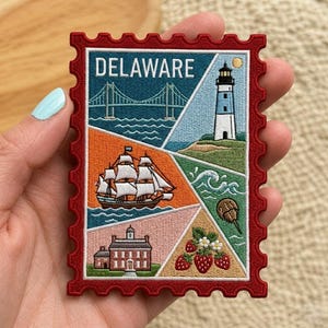 May include: Embroidered patch in the shape of a postage stamp featuring Delaware landmarks. The design includes a bridge, lighthouse, sailboat, historic building, and strawberries, all within a red border.