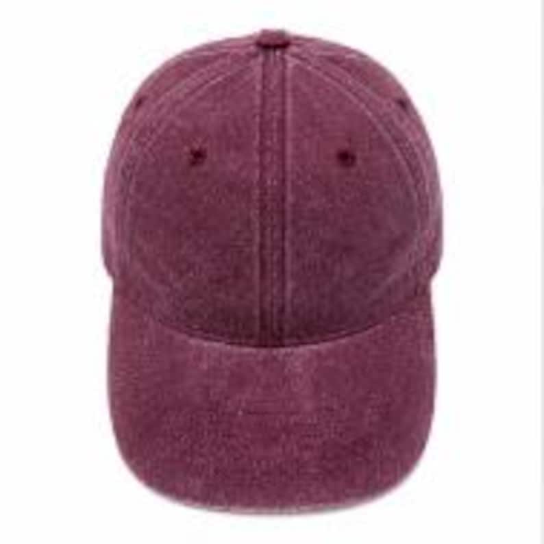 Puede incluir: Una gorra de b&eacute;isbol de color granate oscuro s&oacute;lido con una construcci&oacute;n de seis paneles, una visera curva y un bot&oacute;n cubierto de tela en la parte superior. El material tiene una apariencia ligeramente deste&ntilde;ida y texturizada con ojales.
