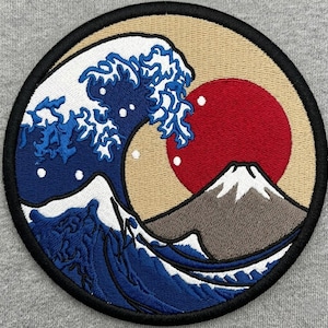May include: Embroidered patch featuring a stylized depiction of a large ocean wave with white crests and dark blue water. A red sun and a mountain are in the background, set against a tan circle with a black border.