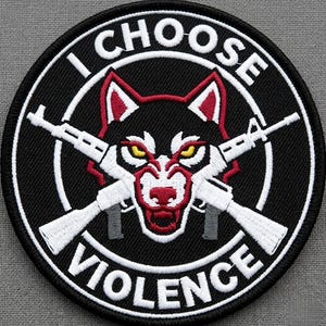 May include: Embroidered patch with the text "I CHOOSE VIOLENCE" in white, encircling a wolf's head with crossed rifles. The wolf has red and white details, with yellow eyes, set against a black background.