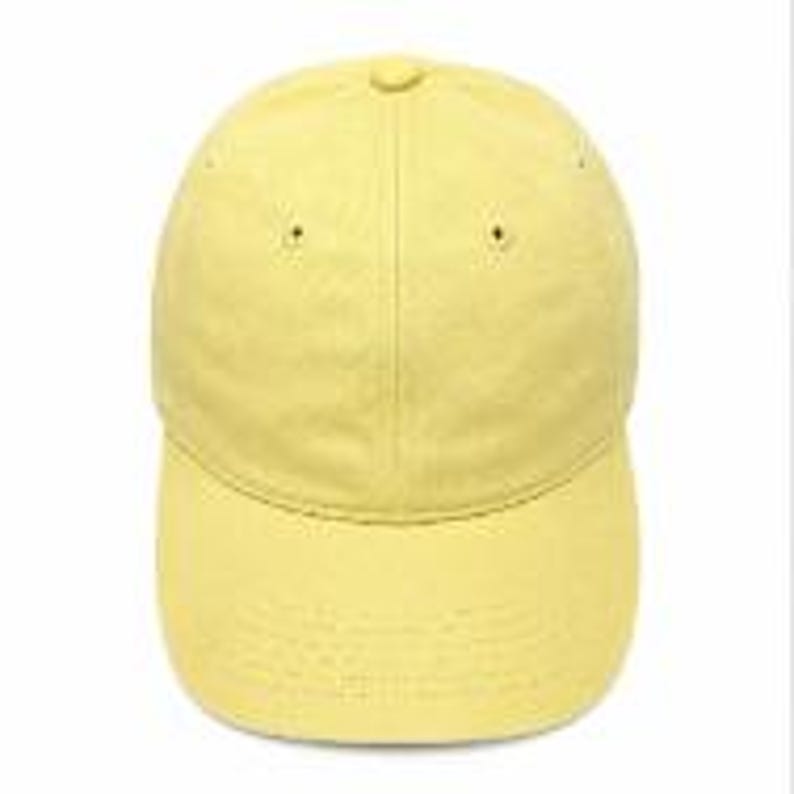 Puede incluir: Una gorra de b&eacute;isbol de color amarillo claro s&oacute;lido que presenta una construcci&oacute;n de seis paneles con visera curva, un bot&oacute;n cubierto de tela en la parte superior y ojales bordados en cada panel para la ventilaci&oacute;n.
