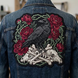 May include: A denim jacket with a large, embroidered patch on the back. The patch features a detailed illustration of a black raven perched atop a pile of bones and skulls, surrounded by red flowers and green vines.