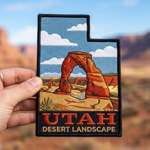 May include: Embroidered patch in the shape of Utah, featuring a desert landscape with a red rock arch under a blue sky with white clouds. The text "UTAH DESERT LANDSCAPE" is at the bottom in orange letters.