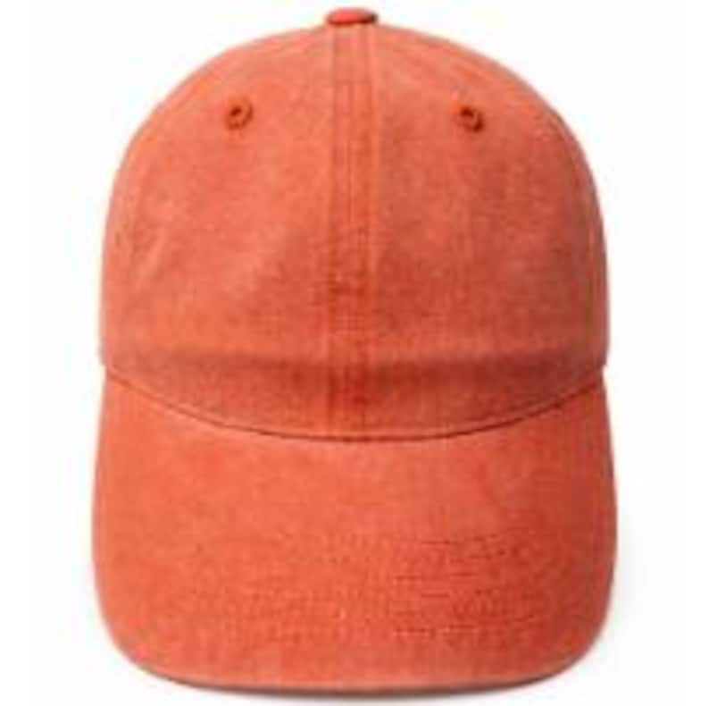 Puede incluir: Una gorra de b&eacute;isbol de color naranja quemado s&oacute;lido con una construcci&oacute;n de seis paneles, una visera curva y un bot&oacute;n en la parte superior. La tela tiene una textura ligeramente desgastada y lavada en toda la corona y la visera, con costuras a juego.