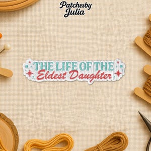 May include: Embroidered patch with the text "THE LIFE OF THE Eldest Daughter" in teal and red. The patch is white with a light blue border and star accents. The patch is surrounded by craft supplies, including thread and scissors.