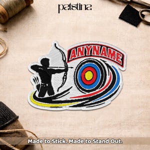 May include: Embroidered patch featuring an archer aiming at a target. The patch includes the text "ANYNAME" in red, a bullseye design, and the words "Made to Stick. Made to Stand Out."
