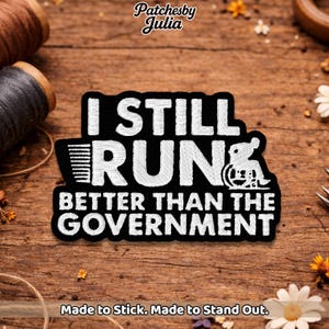May include: Black and white embroidered patch with the text "I STILL RUN BETTER THAN THE GOVERNMENT" and a wheelchair symbol. The patch is rectangular and has a black border. The text "Made to Stick. Made to Stand Out." is at the bottom.