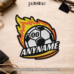 May include: Embroidered patch featuring a soccer ball with the number "00" inside a flame design. The word "ANYNAME" is below the ball. The text "Made to Stick. Made to Stand Out." is at the bottom.