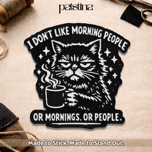 May include: Black embroidered patch featuring a grumpy cat holding a coffee cup. The patch reads "I DON'T LIKE MORNING PEOPLE OR MORNINGS. OR PEOPLE." with stars and the text "Made to Stick. Made to Stand Out."